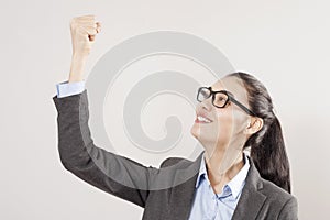 Success in business or career. Enthusiastic businesswoman with raised arms cheering in isolated on grey background