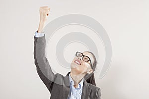 Success in business or career. Enthusiastic businesswoman with raised arms cheering in isolated on grey background