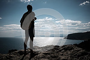 Success concept. Hiker with backpack standing on top of a mountain with raised hands and enjoying view