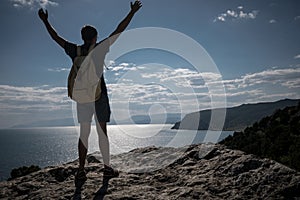 Success concept. Hiker with backpack standing on top of a mountain with raised hands and enjoying view