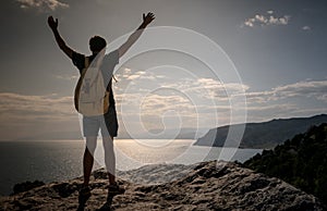 Success concept. Hiker with backpack standing on top of a mountain with raised hands and enjoying view