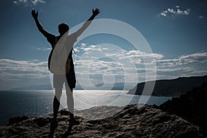 Success concept. Hiker with backpack standing on top of a mountain with raised hands and enjoying view