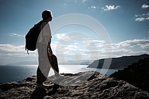 Success concept. Hiker with backpack standing on top of a mountain with raised hands and enjoying view