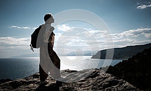 Success concept. Hiker with backpack standing on top of a mountain with raised hands and enjoying view
