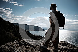 Success concept. Hiker with backpack standing on top of a mountain with raised hands and enjoying view