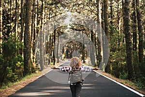 Success and feedom concept with woman and backpack viewed from back and long asphalt road staight in the middle of a high trees