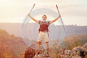 Success Hiker man arms raised with walking pole on the top mountain after hiking to goal walking pole in the sun light .