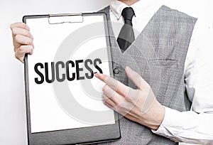 SUCCESS inscription on a notebook in the hands of a businessman on a gray background, a man points with a finger to the text