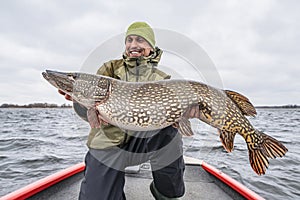 Success pike fishing. Happy fisherman with big fish trophy at boat