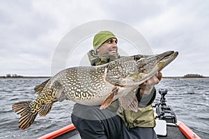 Success pike fishing. Happy fisherman with big fish trophy at boat