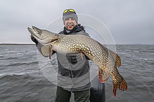 Success pike fishing. Happy fisherman with big fish trophy at boat