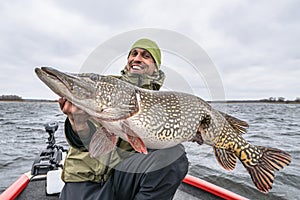 Success pike fishing. Happy fisherman with big fish trophy at boat photo