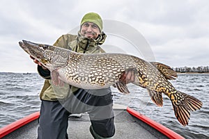 Success pike fishing. Happy fisherman with big fish trophy at boat photo