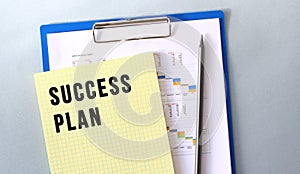 SUCCESS PLAN text written on notepad with pencil. Notepad on a folder with diagrams.