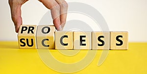 Success process symbol. Businessman turns wooden cubes and changes the word `success` to `process`. Beautiful yellow table, wh