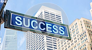 Success road sign, blue color. Highrise buildings and blue sky background