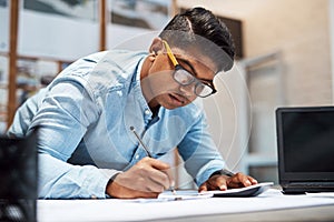 Success is starting to add up. a young architect using a calculator while drawing up a building plan.