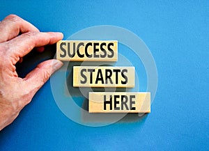 Success starts here symbol. Concept word Success starts here on beautiful wooden block. Businessman hand. Beautiful blue