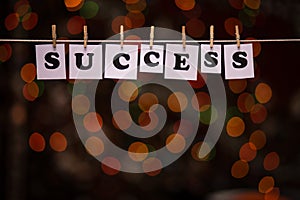 Success text on papers with clothespins with garland bokeh on background