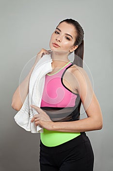 Successful active fit woman wearing sportsuit holding white towel after workout against gray studio wall background