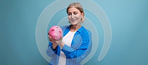 successful adult business woman with money piggy bank on blue background with copy space