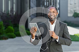 Successful african american boss outside office building with tablet computer and headphones talking remotely with