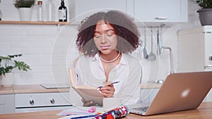 Successful African American female taking notes in workbook looking at laptop