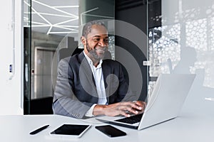 Successful african american manager inside office at workplace, man working using laptop smiling and happy with