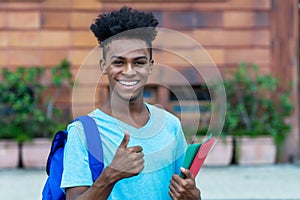 Successful afro american male student with backpack and paperwork showing thumb up