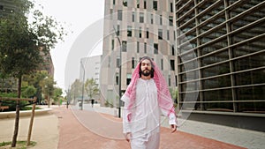 Successful arab man sheikh in traditional clothes looking at skyscrapers while walking city street