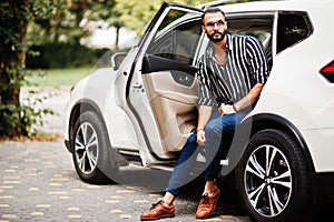 Successful arab man wear in striped shirt and sunglasses pose near his white suv car.