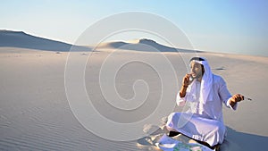 Successful Arabian Sheikh businessman communicates on smartphone with business partner sitting on sand with drawing in