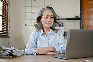 Successful Asian aged businesswoman sitting at her office desk