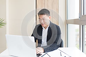 Successful Asian businessman, in a business suit, works on a laptop, relaxes in a stylish office