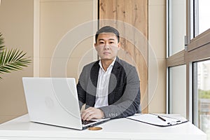 Successful Asian in a business suit, works on a laptop, relaxes in a stylish office