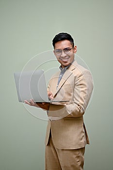 Successful Asian businessman holding his laptop, standing against green studio background