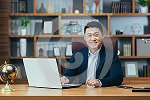 successful Asian businessman, man working in the office sitting at the table, looking at the camera and smiling,