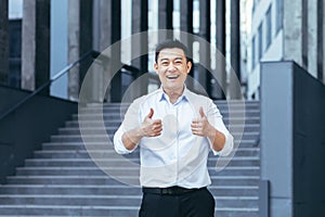 Successful asian businessman outside office smiling, thumbs up affirmatively