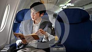 Successful Asian businessman reading a book during the flight for his business trip