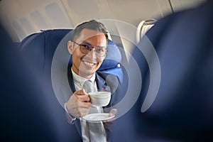 Successful Asian businessman sits at the window seat sipping coffee during the flight