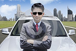 Successful Asian businessman wearing sunglasses in front of luxury car