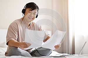 Successful asian businessman working from home, using laptop, headset