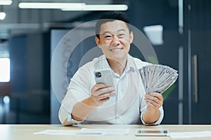 Successful asian businessman working in office, man smiling and looking at camera
