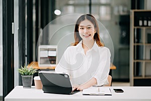 Successful Asian Businesswoman Analyzing Finance on Tablet and Laptop at modern Office Desk tax, report, accounting, statistics,