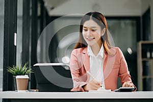 Successful Asian Businesswoman Analyzing Finance on Tablet and Laptop at modern Office Desk tax, report, accounting, statistics,