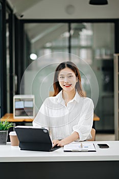 Successful Asian Businesswoman Analyzing Finance on Tablet and Laptop at modern Office Desk tax, report, accounting, statistics,