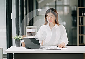 Successful Asian Businesswoman Analyzing Finance on Tablet and Laptop at modern Office Desk tax, report, accounting, statistics,