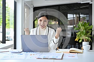 Successful Asian businesswoman celebrating at her office desk