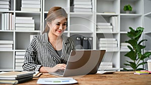 A successful Asian businesswoman responding to emails on her laptop at her desk