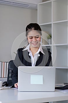 Successful Asian businesswoman sitting in modern office Use a calculator and laptop to calculate tax and finance.